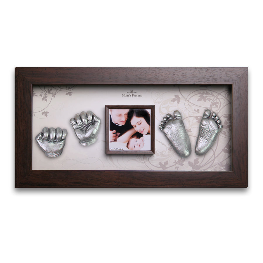 A LOVE MOM'S PRESENT Momspresent Baby Hands and Foot 3D Casting Print DIY Kit with Walnut Frame6. Autumn-flavor showcases two sets of silver-colored plaster casts of a baby's hands and feet, artistically arranged around a small photo of a loving couple with their baby. Mounted on a patterned background, the frame features a plaque reading "Mom's Present," making it an ideal luxury baby gift.