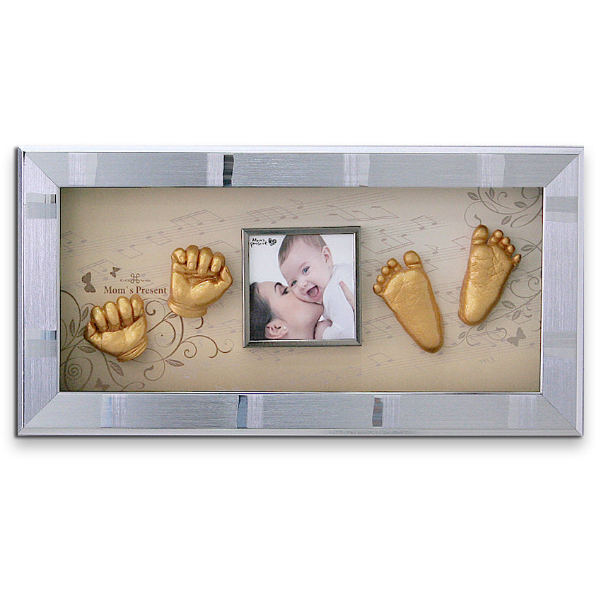 A decorative frame featuring a central photo of a mother kissing her baby, surrounded by golden casts of the baby's hands and feet. The frame has musical notes, a floral design, and can be created using the LOVE MOM'S PRESENT Momspresent Baby Hands and Foot 3D Casting Print DIY Kit with SILVER Frame3-piano concerto for that perfect personal touch.