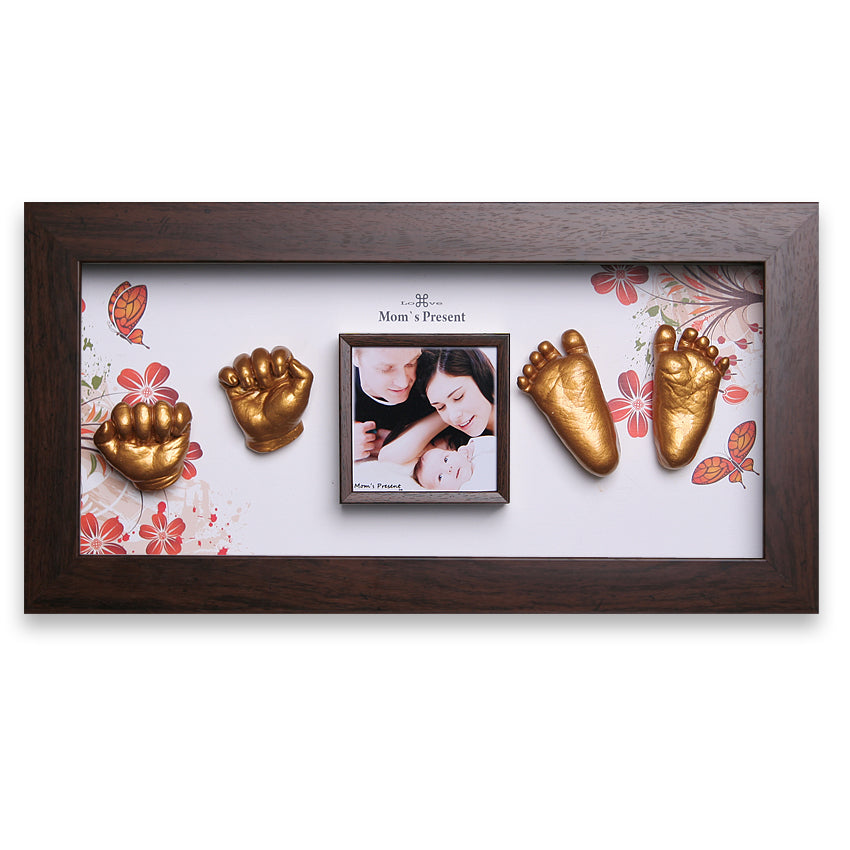 A framed display with a central photo of a couple and their baby. Surrounding the photo are golden casts of baby hands and feet, arranged symmetrically. The background has floral patterns, and a title above the photo reads, "Mom's Present." This custom baby gift creates a luxury baby memory kit: the LOVE MOM'S PRESENT Momspresent Baby Hands and Foot Casting 3D Print DIY Kit with Walnut Frame1- The spring of life.