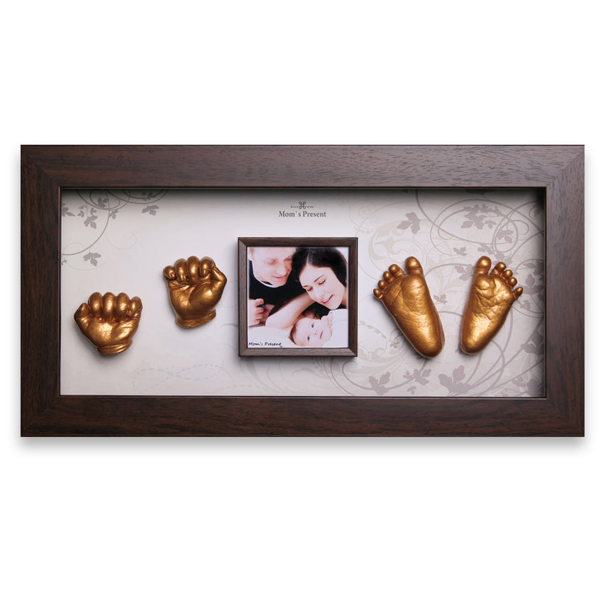 A rectangular dark wooden frame displays a photo of a couple with their baby, positioned centrally. Surrounding the photo are gold casts of two baby hands and two baby feet, arranged symmetrically on a decorative white and gray floral background. This LOVE MOM'S PRESENT Momspresent Baby Hands and Foot 3D Casting Print DIY Kit with Walnut Frame makes for an elegant memory frame and a luxury baby gift.