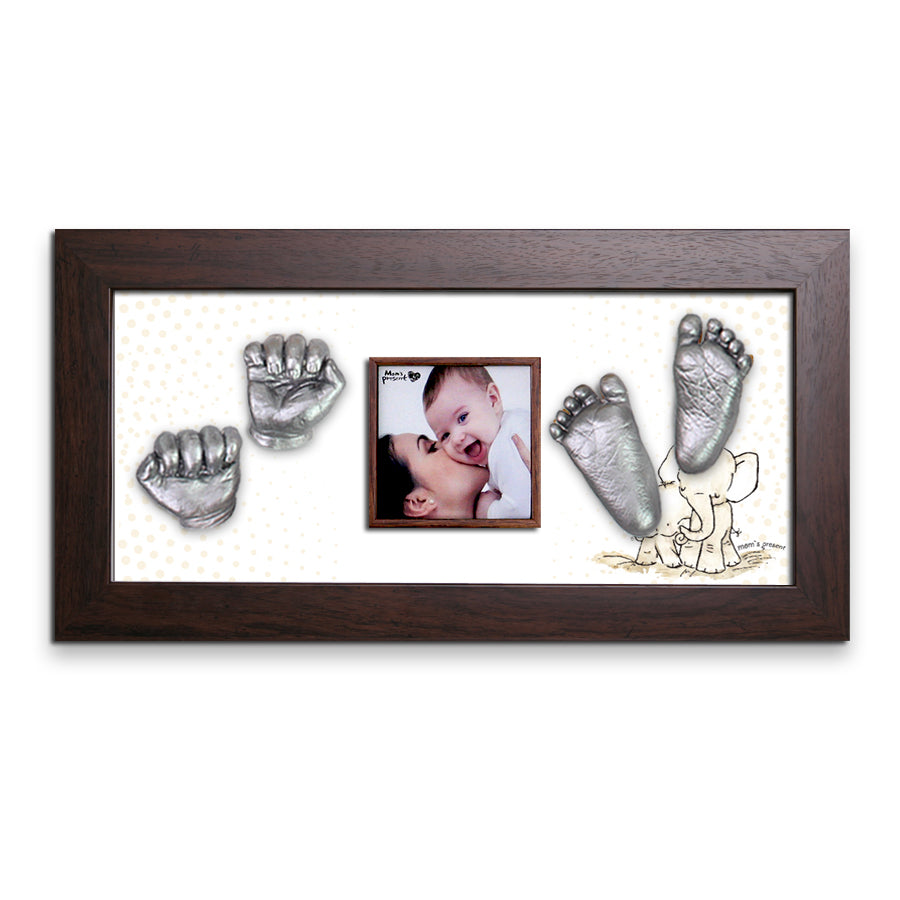 A luxury photo frame features a baby being kissed on the cheek. Surrounding the photo are silver 3D molds of baby hands and feet from a Momspresent Baby Hands and Foot 3D Casting Print DIY Kit with Walnut Frame8-Elephant-Hug. The background includes a subtle polka dot pattern, with an adorable illustration of an elephant in the lower right corner, perfect as LOVE MOM'S PRESENT.