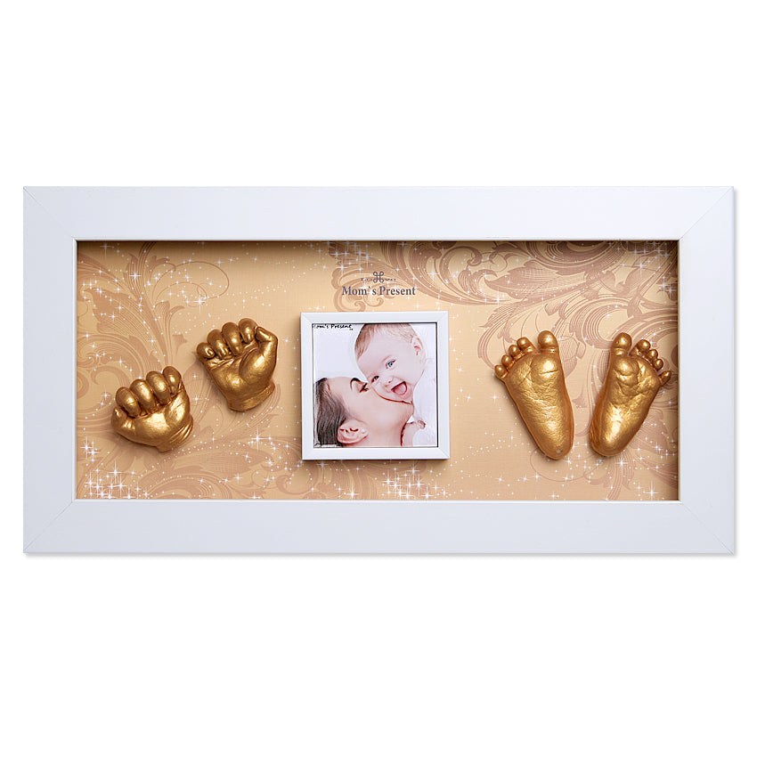 White rectangular picture frame displaying a photo of a mother kissing a baby, flanked by golden casts of tiny hands on the left and tiny feet on the right against an ornate cream background. Text at the top reads "Momspresent Baby Hands and Foot 3D Casting Print DIY Kit with White Frame2-The age of gol." The arrangement gives it the look of an elegant baby handprint and footprint kit from LOVE MOM'S PRESENT.